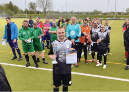 Ein Spieler der Fußballmannschaft der Stralsunder Werkstätten steht vor seinem Team und hält einen Pokal und die Urkunde in den Händen.