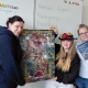 Drei Personen zeigen ein fertiges Puzzle mit Dinosauriermotiv und ein Fachbuch.