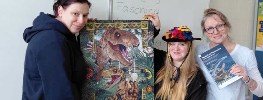Drei Personen zeigen ein fertiges Puzzle mit Dinosauriermotiv und ein Fachbuch.