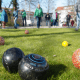 Im Vordergrund liegen verschiedenfarbige Kugeln während eines Rasenbowlingspiels. Im Hintergrund sind viele Spieler zu sehen.