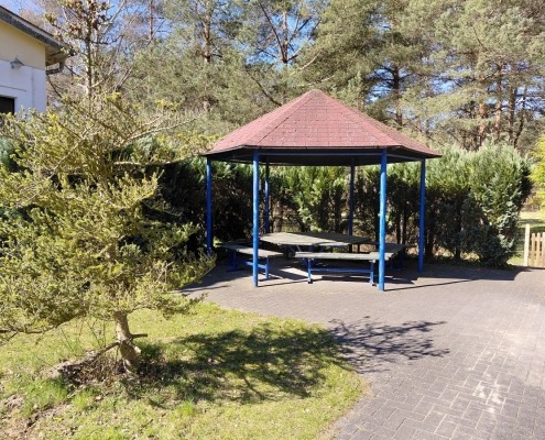 Im Außenbereich der Tagesgruppe für Senioren steht ein Holzpavillon mit einem Tisch und Sitzbänken.