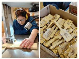 Eine Frau arbeitet an einer Bandsäge. Daneben sind die fertiggestellten Kinderklappern zu sehen.
