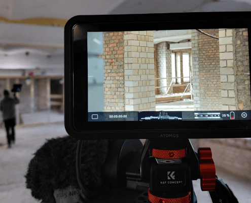 Das Foto zeigt den Blick auf den Bildschirm einer Filmkamera. Auf dem Bildschirm sind unverputzte Wände einer Baustelle zu sehen.