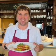 Bistro_Delikater_Servicepersonal Eine Person serviert im Bistro ein Mittagsgericht.