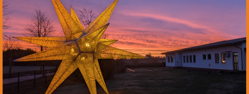 Ein 7 Meter hoher Stern vor der Hauptwerkstatt der Stralsunder Werkstätten leuchtet in orange.