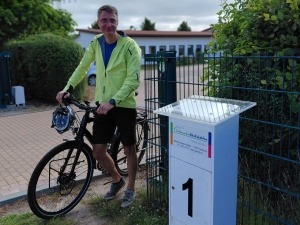 Ein Mann steht mit seinem Fahrrad neben einem Schild, auf dem die Zahl 1 abgebildet ist.