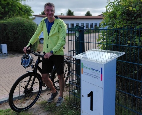 Ein Mann steht mit seinem Fahrrad neben einem Schild, auf dem die Zahl 1 abgebildet ist.