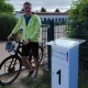 Ein Mann steht mit seinem Fahrrad neben einem Schild, auf dem die Zahl 1 abgebildet ist.