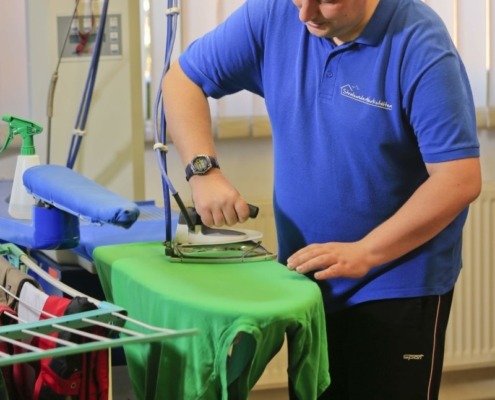 Eine Person bügel ein T-Shirt am Bügelbrett.